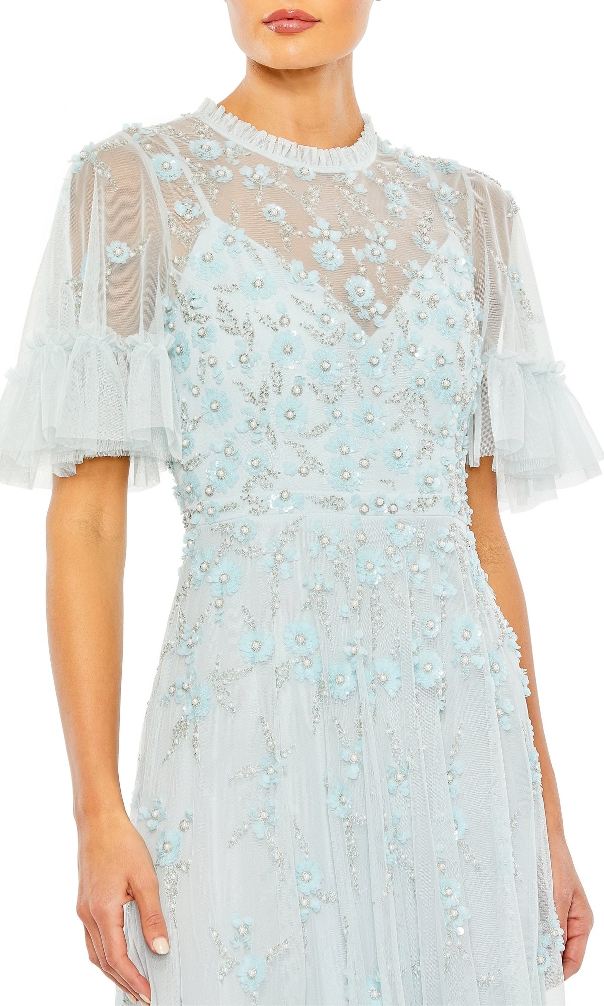 A woman wears the Mac Duggal 9199 Short Sleeve Beaded Formal Gown in light blue, featuring short ruffled sleeves, floral appliqué, beading, and a high ruffled neckline—an elegant long A-line evening dress.